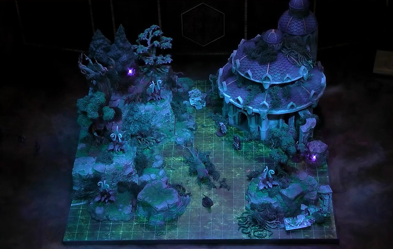 A battlemap of an outdoor space with trees on rocky hills on the left and a large dome-roofed building on the right. Two armored guards stand by the entrance of the building and a black-furred four-legged animal walks in the foreground. The building has a three-tiered roof, a tower with cupola behind it, and a glowing purple light within a stone structure next to it. Among the trees are tall white fiddlehead-like plants, one thick tree with no leaves at the top, and a glowing purple light.