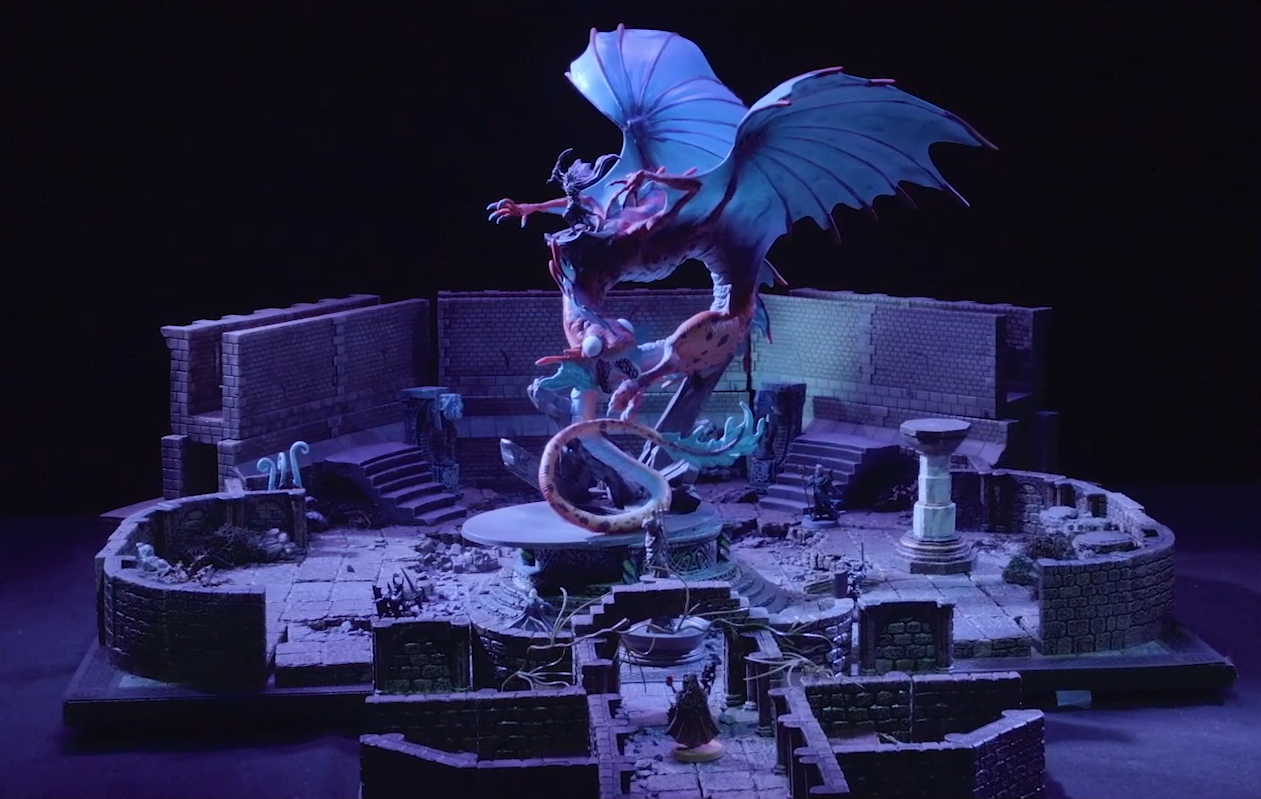 A battlemap of a stone chamber, in the center of which is Gloamglut, a massive snake-like dragon. Its wings are outstretched and on its back is Sorrowlord Zathuda in black armor holding a sword aloft. The large, blank white eyes of Gloamglut’s fish-like head look forward, its split lower jaw open and filled with sharp teeth. Fearne stands alone at the end of a long hallway in front of it.