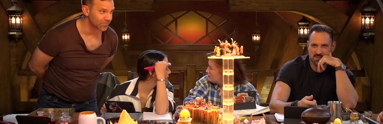 Liam, Laura, Ashley, and Travis sit at the table. A transparent plastic platform with several miniatures placed on top of it is visible in the foreground.