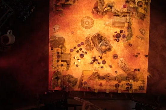 A top-down view of a battlemap of a large outdoor space filled with stone walls and parts of buildings. In the center is a tower with a pale white globe at the top. A number of combatants fill the area on the ground and atop the walls.