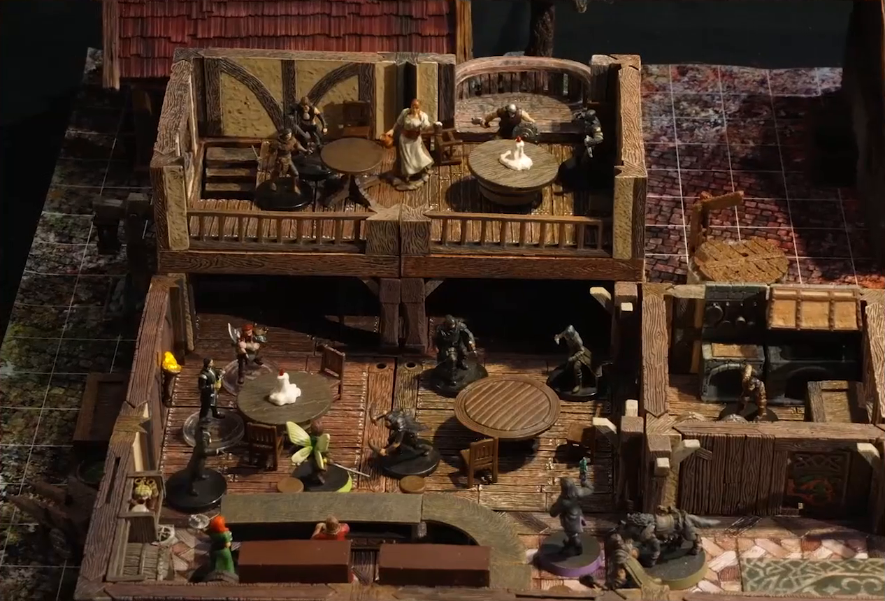 A battlemap of the interior of a wooden tavern. A number of black-cloaked individuals and other rogues stand near round tables, facing off against Thimble, Occtis, Kattigan, and Wulfric. Two bartenders, one thin and in a green dress, one stout and burly, stand behind a countertop. A small side room houses brick stoves, barrels, and a long-armed, beast-like individual. An upper level of the tavern has more tables, rogues, and an individual in a white dress who appears to be a server. A covered well sits outside the tavern.