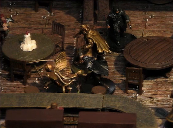 A battlemap of the interior of a wooden tavern focused on Kattigan and Thimble facing off against two black-robed individuals and a red-bearded dwarf holding an axe. They fight amongst round tables, one of which has a melting white candle in the center. A bartender watches from the other side of a counter.