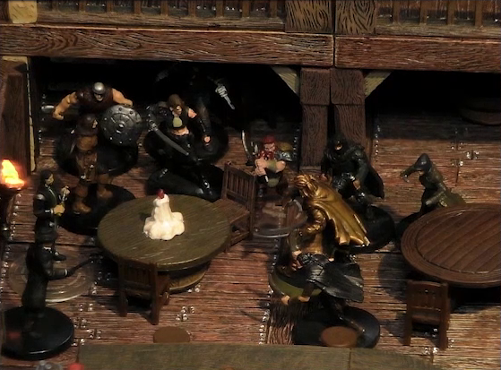 A battlemap of the interior of a wooden tavern focused on Kattigan facing off against ten black-robed individuals and other rogues. They fight amongst round tables, one of which has a melting white candle in the center. The railing of an upper level is visible in the background.