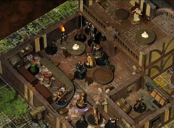 A battlemap of the interior of a wooden tavern. A number of black-cloaked individuals and other rogues stand near round tables, facing off against Occtis, Kattigan, Wulfric, and Vaelus. Vaelus stands on a counter, behind which are two bartenders, one thin and in a green dress, one stout and burly. A small side room houses brick stoves, barrels, and a long-armed, beast-like individual. An upper level of the tavern has more tables and an individual in a white dress who appears to be a server.