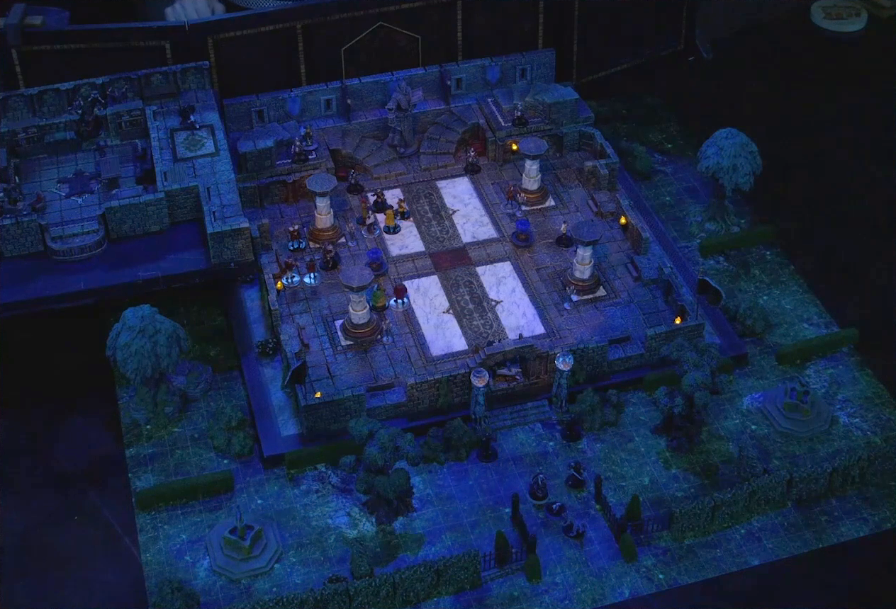 A battlemap of a stone palace split into two levels, surrounded by a courtyard. Vaelus, Julien, Pincushion, and Thaisha in wolf form stand outside the palace entrance, just inside the open gate. Downstairs is a marble floor, marble pillars, and twin staircases curving up on either side of a large robed statue holding a lantern and open book. A number of people are scattered throughout the downstairs space. Upstairs is a hallway leading past a room with a bearskin rug, balcony, and wooden table, next to which is Occtis. A number of robed individuals including Ethrand Tachonis gather outside the room, down the hall from a fallen guard. Two black-clothed individuals stand outside the entrance to the palace next to two pillars topped with large spherical crystals. The rest of the courtyard contains trees, two fountains, and an open gate leading in.