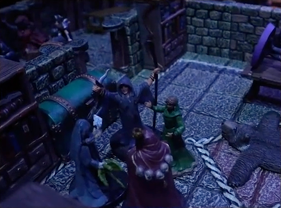 A battlemap of a stone palace room focused on three robed individuals facing off against Aranessa. One individual wields a curved knife and long staff. Another in a maroon robe has skulls draped across his back. Aranessa wears a green dress. At the edge of the image, Occtis lays on a stone table. A bearskin rug is on the ground nearby. Thaisha and more robed individuals are outside the room in a hallway.