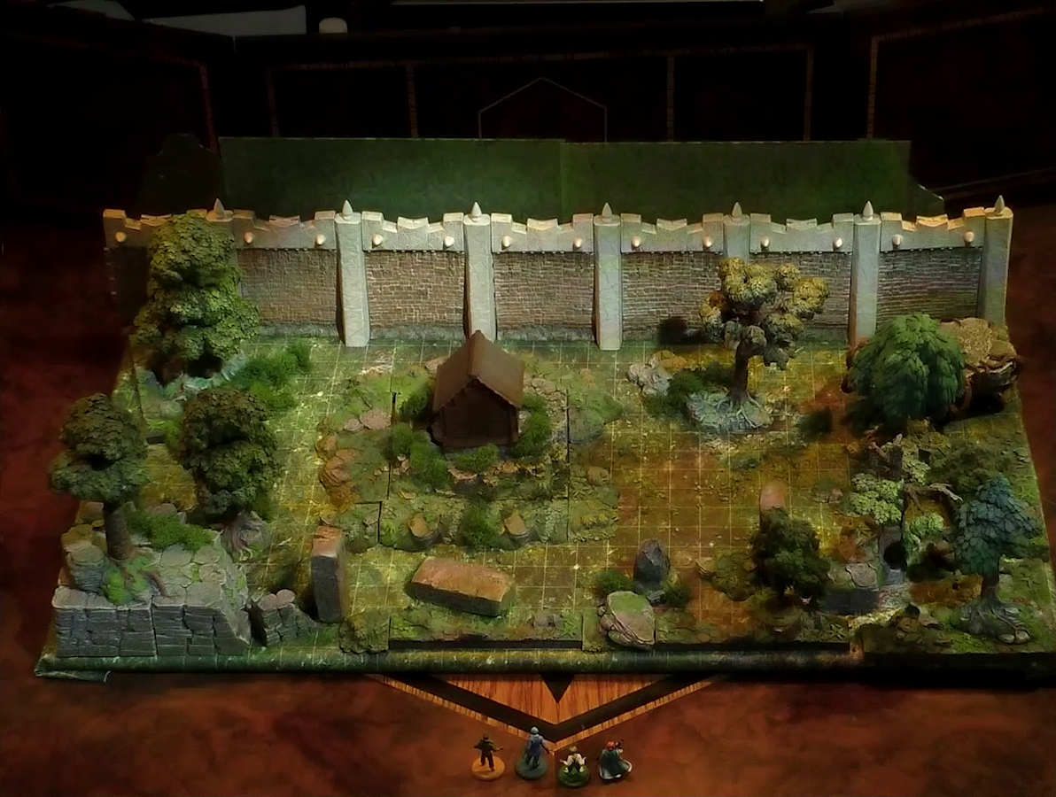 A battlemap of a wooded courtyard bordered on one side by a tall stone defensive wall. A translucent blue magic-looking barrier tops the wall. A small wooden shed sits among some bushes in the center of the courtyard. Filling the rest of the space are trees and old-looking standing stones with circular runic patterns carved into their sides. Kai, Jessep, Padmund, and Sky stand just off the edge of the battlemap looking in.