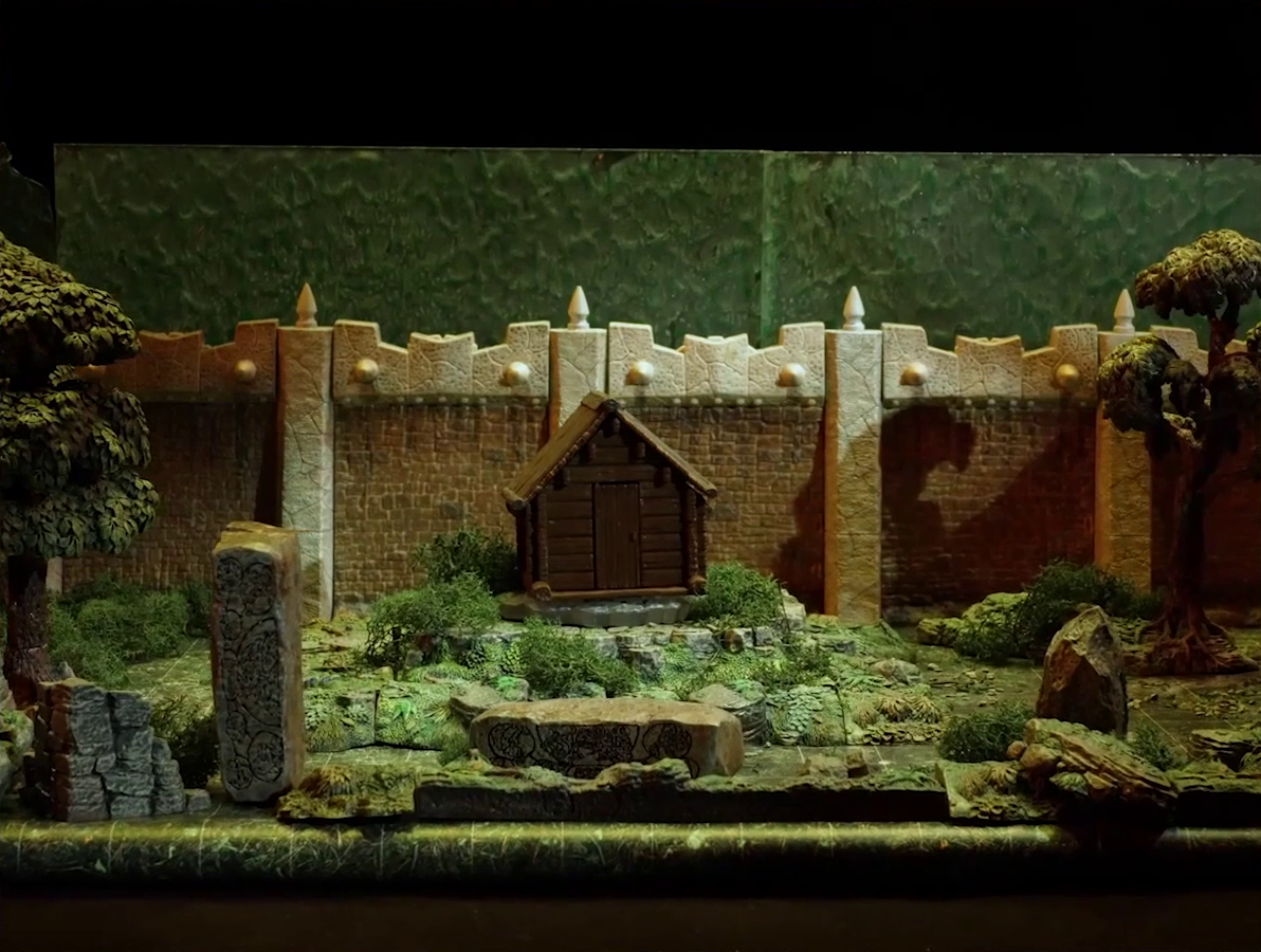 A battlemap of a wooded courtyard bordered on one side by a tall stone defensive wall. A translucent blue magic-looking barrier tops the wall. A small wooden shed sits among some bushes in the center of the courtyard. Filling the rest of the space are trees and old-looking standing stones with circular runic patterns carved into their sides.