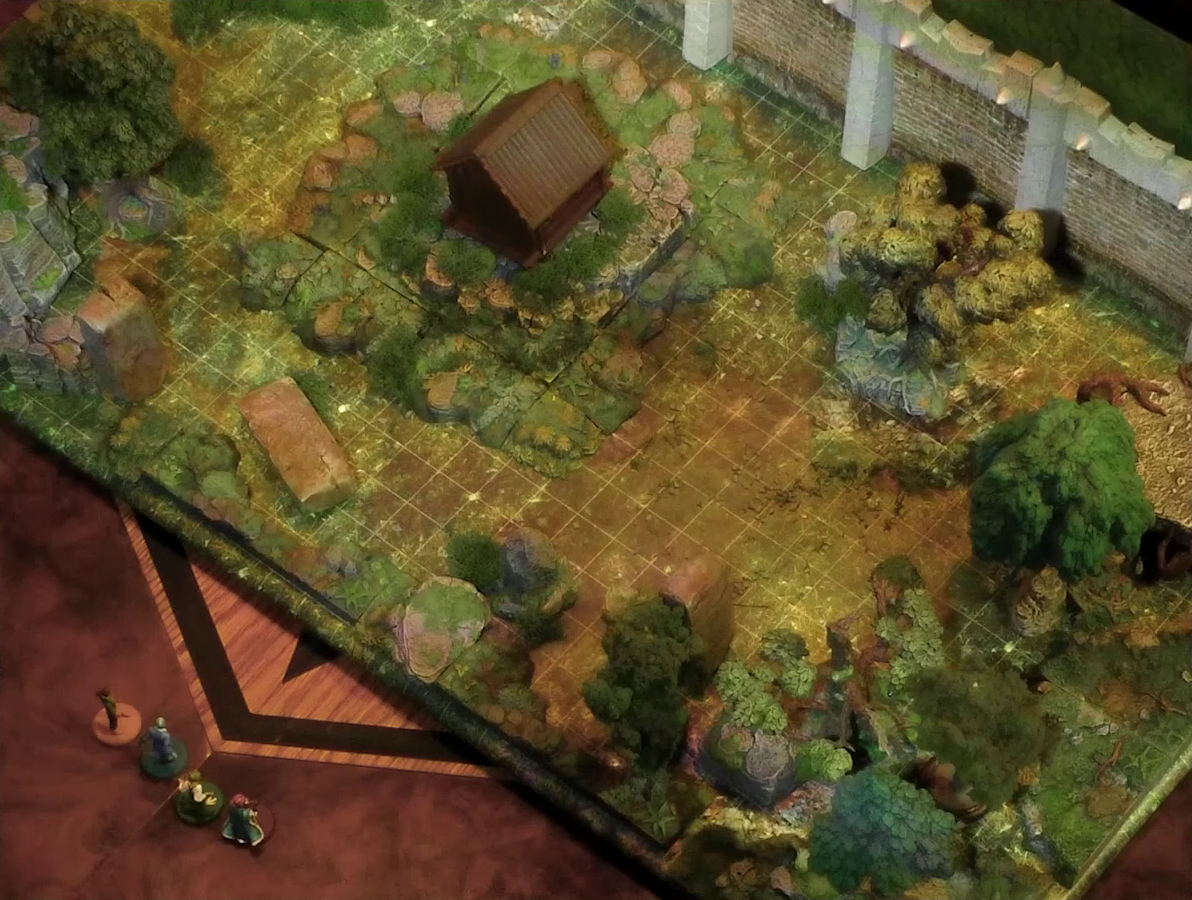 A battlemap of a wooded courtyard bordered on one side by a tall stone defensive wall. A translucent blue magic-looking barrier tops the wall. A small wooden shed sits among some bushes in the center of the courtyard. Filling the rest of the space are trees and old-looking standing stones with circular runic patterns carved into their sides. Kai, Jessep, Padmund, and Sky stand just off the edge of the battlemap looking in.
