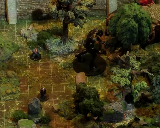 A close-up of a battlemap showing a section of a wooded courtyard with a stone defensive wall at the top edge of the image. Three monsters are in this space. One is a large jet-black humanoid with no clothing and no discernable face, lurching forward with its hands out. The second is a small ball-shaped creature with its torso split open in a toothy maw, two clawed hands emerging from its headless body. The third is a small up-right creature with a cone-like head.