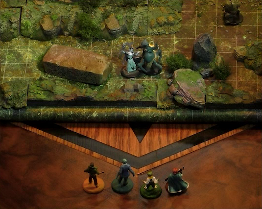 A close-up of the edge of a wooded battlemap. Kai, Jessep, Padmund, and Sky stand just off the battlemap looking in. Three monsters are on the battlemap. One is a small reptilian creature standing on two clawed feet with spines running down its back. The second has teal skin and four spider-like legs propping up a torso with two arms and a rodent-like head. The third seems to be a robed humanoid surrounded by thick translucent strands. A fallen standing stone with circular runic patterns carved into its side is near the monsters.