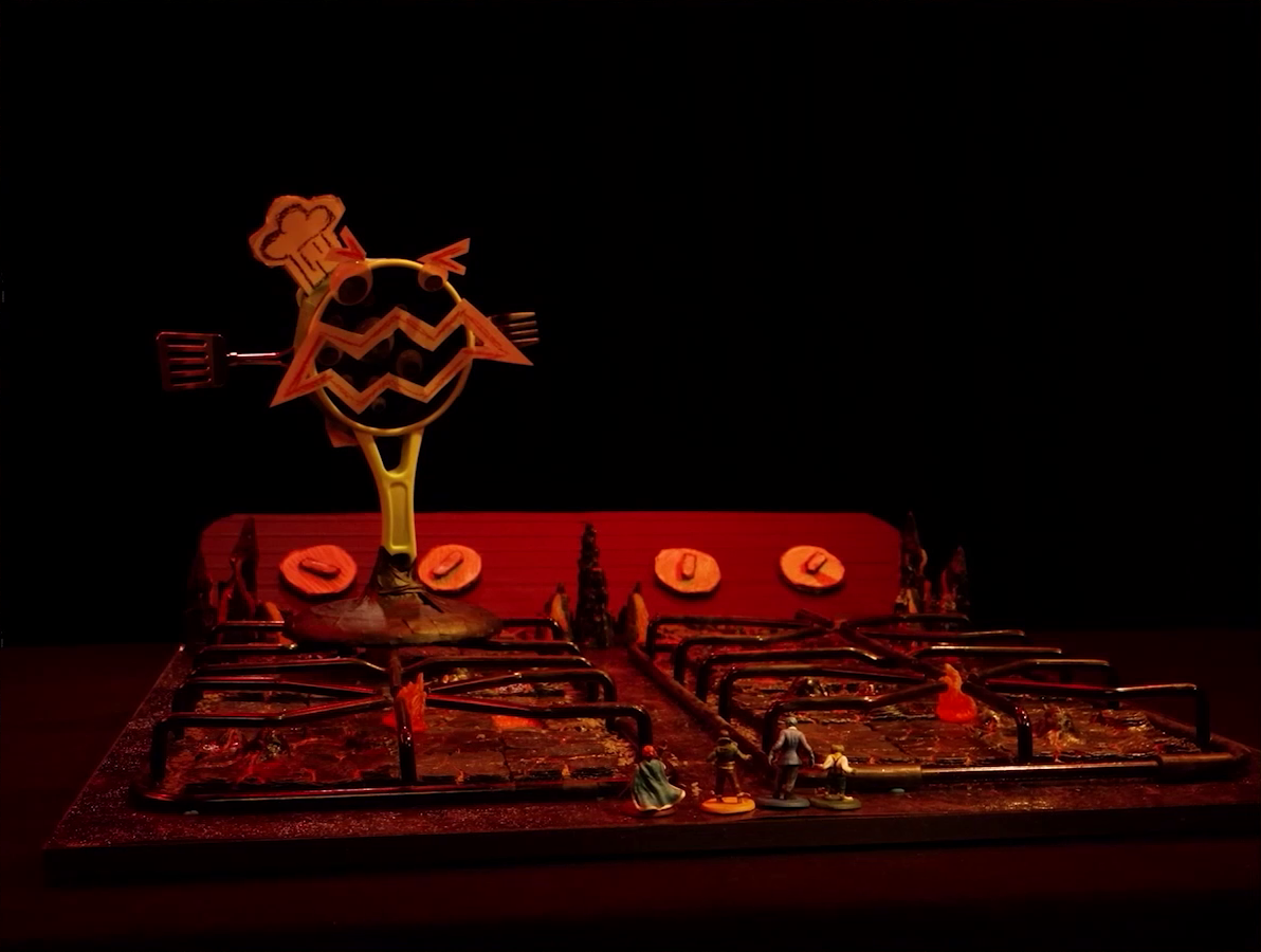 A battlemap that looks like a stovetop. Small flames sprout from each of the four burners and four knobs are on the back panel. Wok Wok, the giant frying pan creature, is on the back left burner. Sky, Kai, Jessep, and Padmund stand at the front of the battlemap and Yasha and Beau stand at the back. The base of the battlemap looks like magma and the scene is bathed in red light.