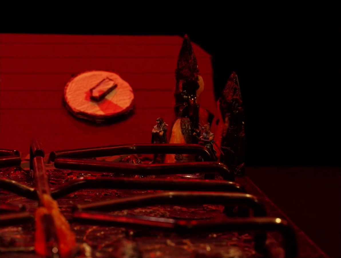 A close-up of a battlemap that looks like a stovetop. Yasha and Beau stand at the back behind the burners and in front of a knob on the back panel. Fire rises up behind them.