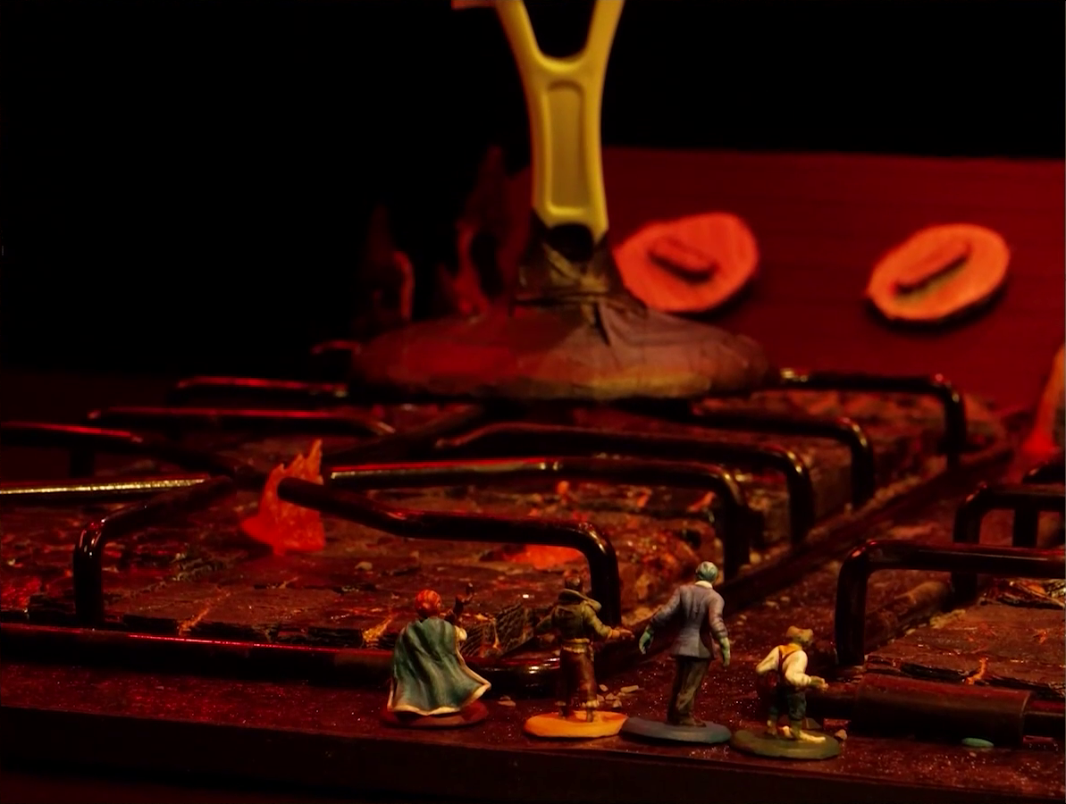 A close-up of a battlemap that looks like a stovetop. Sky, Kai, Jessep, and Padmund stand at the front. Before them are burners with flames emerging from the center and the base of a giant frying pan creature. Two knobs are visible on the stove’s back panel in the background.