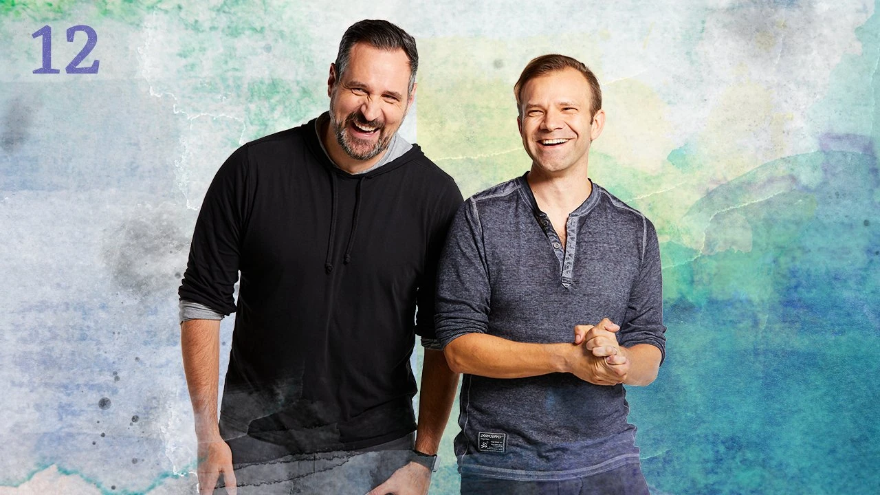 Thumbnail for episode 12. Travis and Liam pose smiling side-by-side. Liam’s hands are clasped in front of him. They are dressed in black and gray and stand against a colorful backdrop with splashes of greens, blues, and yellows over white.