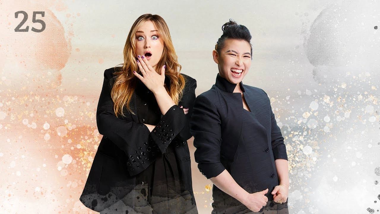 Thumbnail for episode 25. Ashley and Erika Ishii pose side-by-side. Ashley looks surprised, he hand resting under an open mouth. Erika is grinning widely with their hands at their waist. They are dressed in black and stand against a colorful backdrop with splashes of oranges on the left and muted grays on the right, with white underneath.