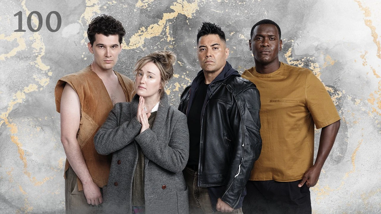 Thumbnail for episode 100. Nick Marini, Ashley, Noshir Dalal, and Abubakar Salim pose in a line. Ashley’s hands are in front of her in prayer. Nick wears an open brown vest with no undershirt, Ashley wears a long gray jacket, Noshir wears a black leather jacke, and Abubakar wears a yellow fabric shirt. They stand against a colorful backdrop with golden streaks over a black and white base, looking like veins of ore through rock.