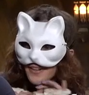 A person in a white cat mask covering the upper half of their face. They are looking forward with a slight smile.