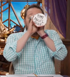 Sam drinking from a silver chalice with the text “YUMMY ANGEL BLOOD” written on the bottom in black marker. Splotches of red resembling blood are below the text. Sam holds the chalice with two hands as he tips it fully horizontally into his mouth.