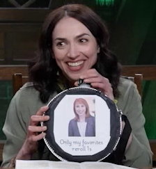 A circular canteen with a screw top. An image of a smiling woman with shoulder length red hair over the text “Only my favorites reroll 1s” is printed on a white sheet of paper taped to the front. Eden Riegel holds it, smiling.