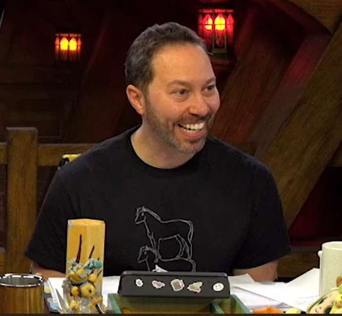 Sam wearing a black T-shirt with a white line drawing of a horse standing on another horse’s back. Sam is giving a toothy grin.